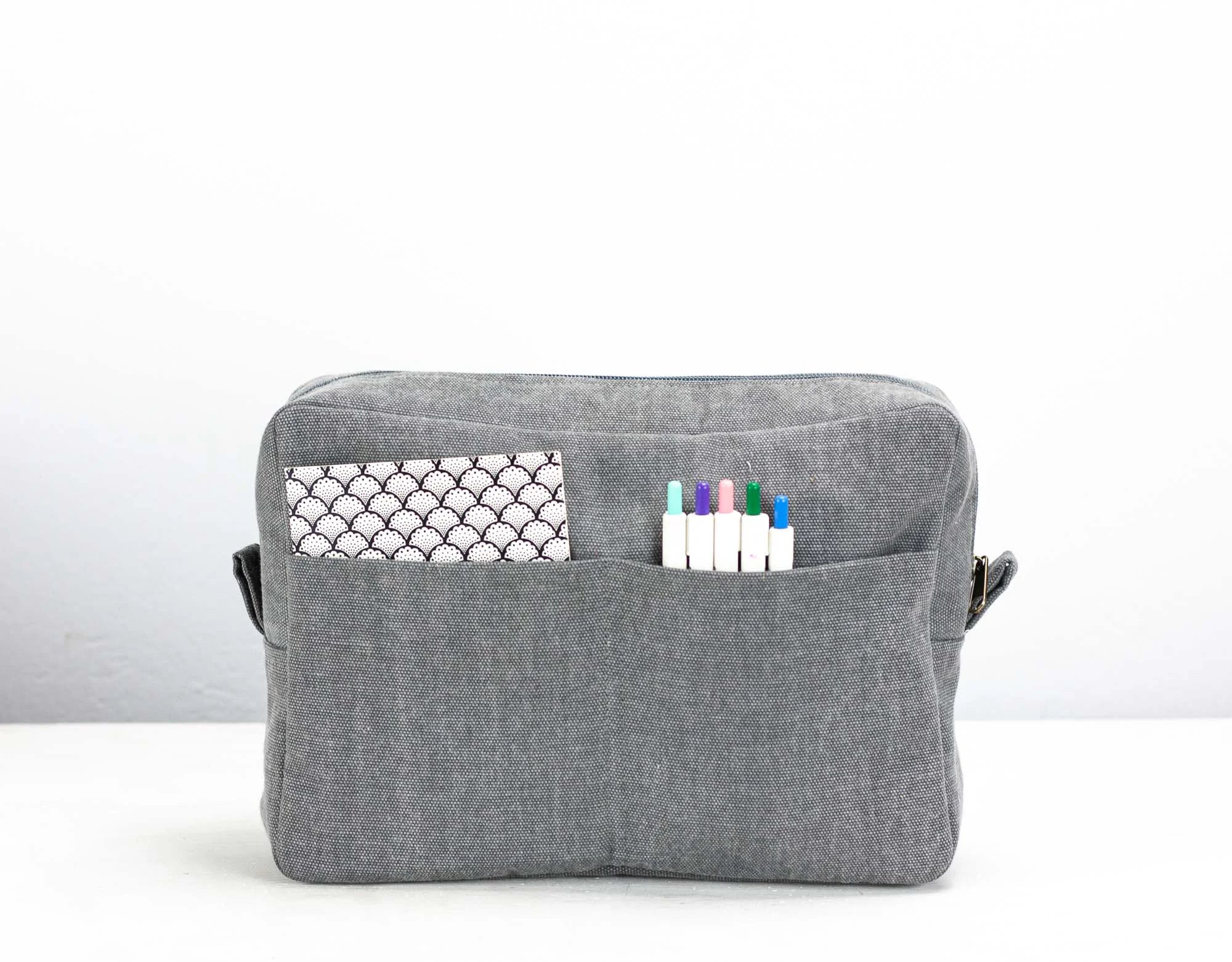 Gray fabric pouch with a pocket and markers on a white background