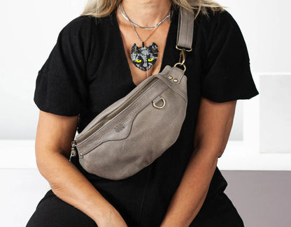 Person wearing a black shirt with a gray sling bag and a necklace with a cat pendant.