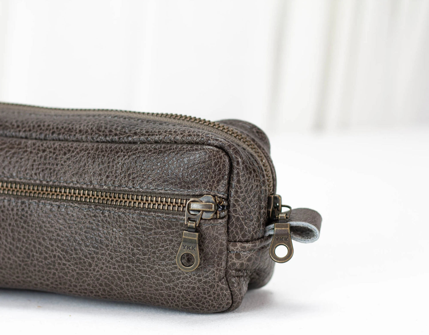Close-up of a gray leather pouch with a zipper on a white background