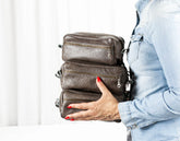 Person holding a stack of grey handbags against a white background