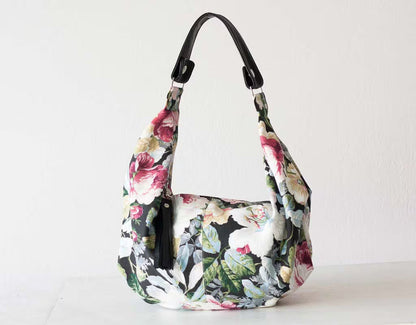 Floral patterned handbag with a black strap on a white background