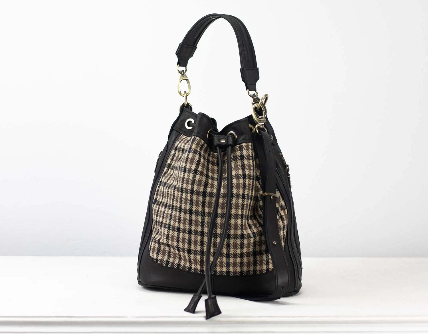 Handbag with plaid pattern and black leather accents on a white background