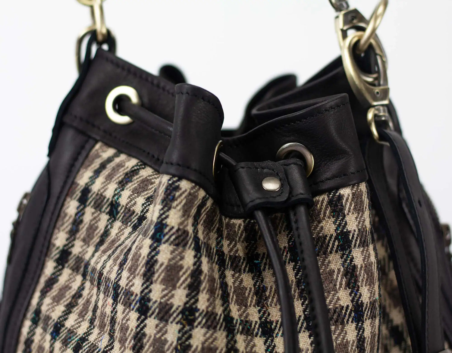 Close-up of a plaid handbag with black straps and gold hardware.