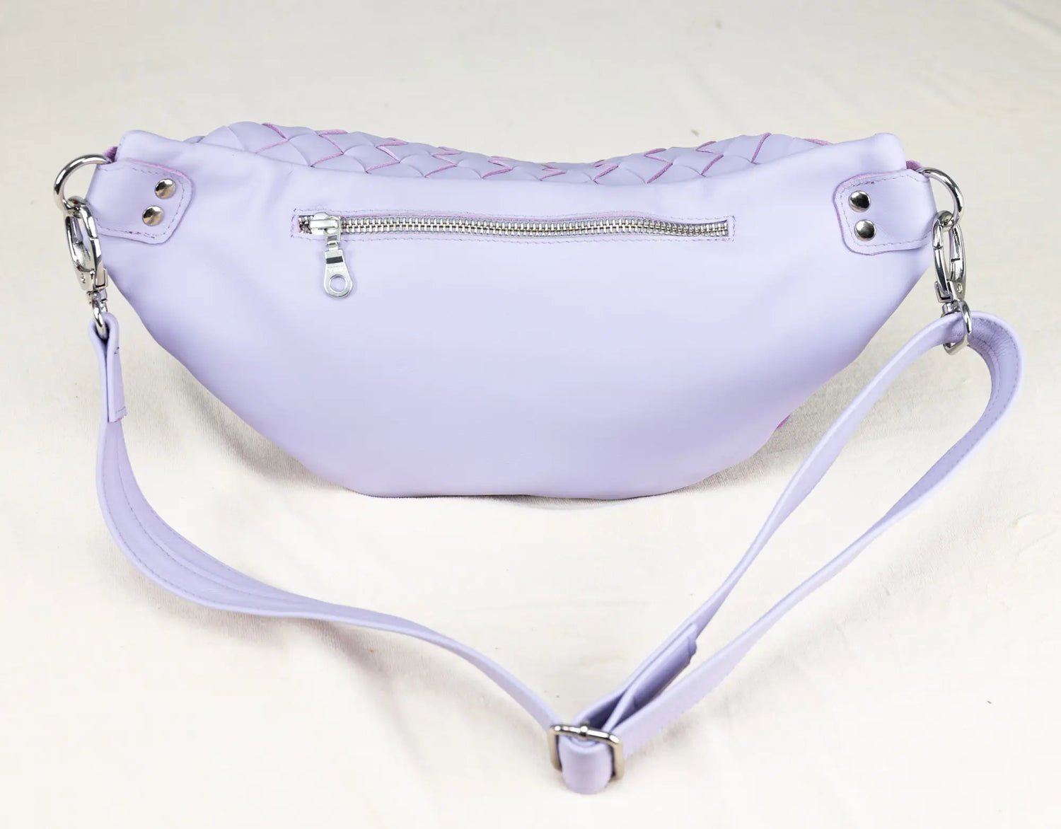 Lavender waist bag with braided top and zippers on a light gray background