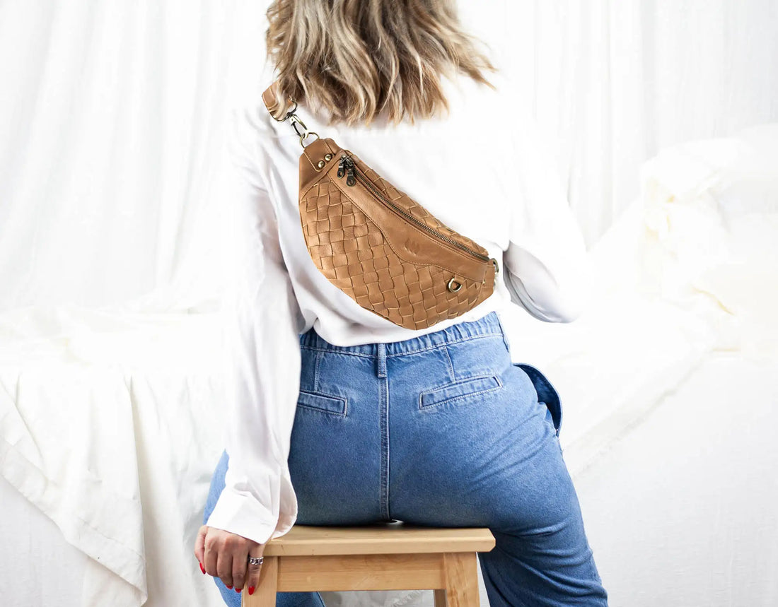 Person wearing a brown woven fanny pack over a white shirt and blue jeans on a white background