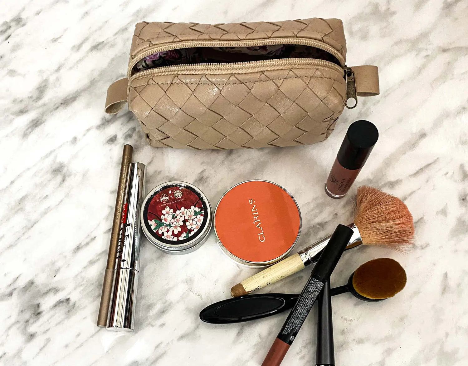 Makeup bag with makeup items on a marble surface