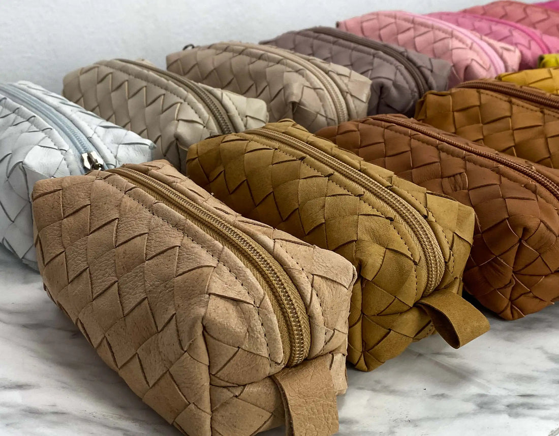 Row of woven makeup bags in various colors on a marble surface