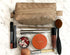 Makeup items including a Clarins product, lip gloss, and brushes on a marble surface with a woven beige pouch.
