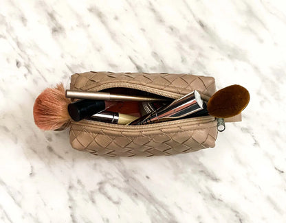 Beige woven makeup bag with cosmetic items on a marble surface