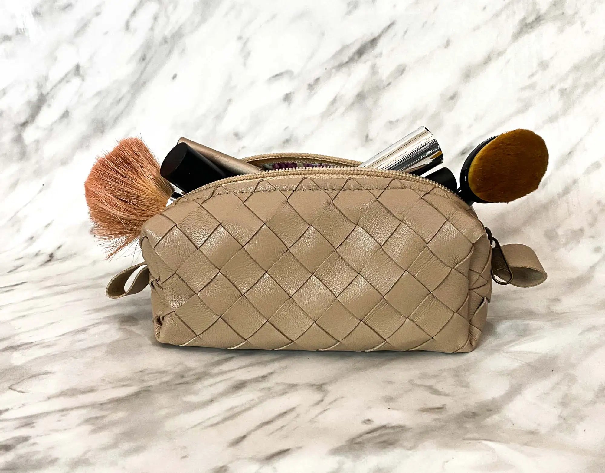 Beige woven makeup bag with brushes on a marble background
