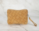 Tan woven clutch bag with a strap on a light marble background