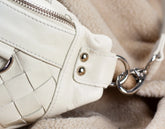 Close-up of a white woven handbag with a chain detail on a soft beige background