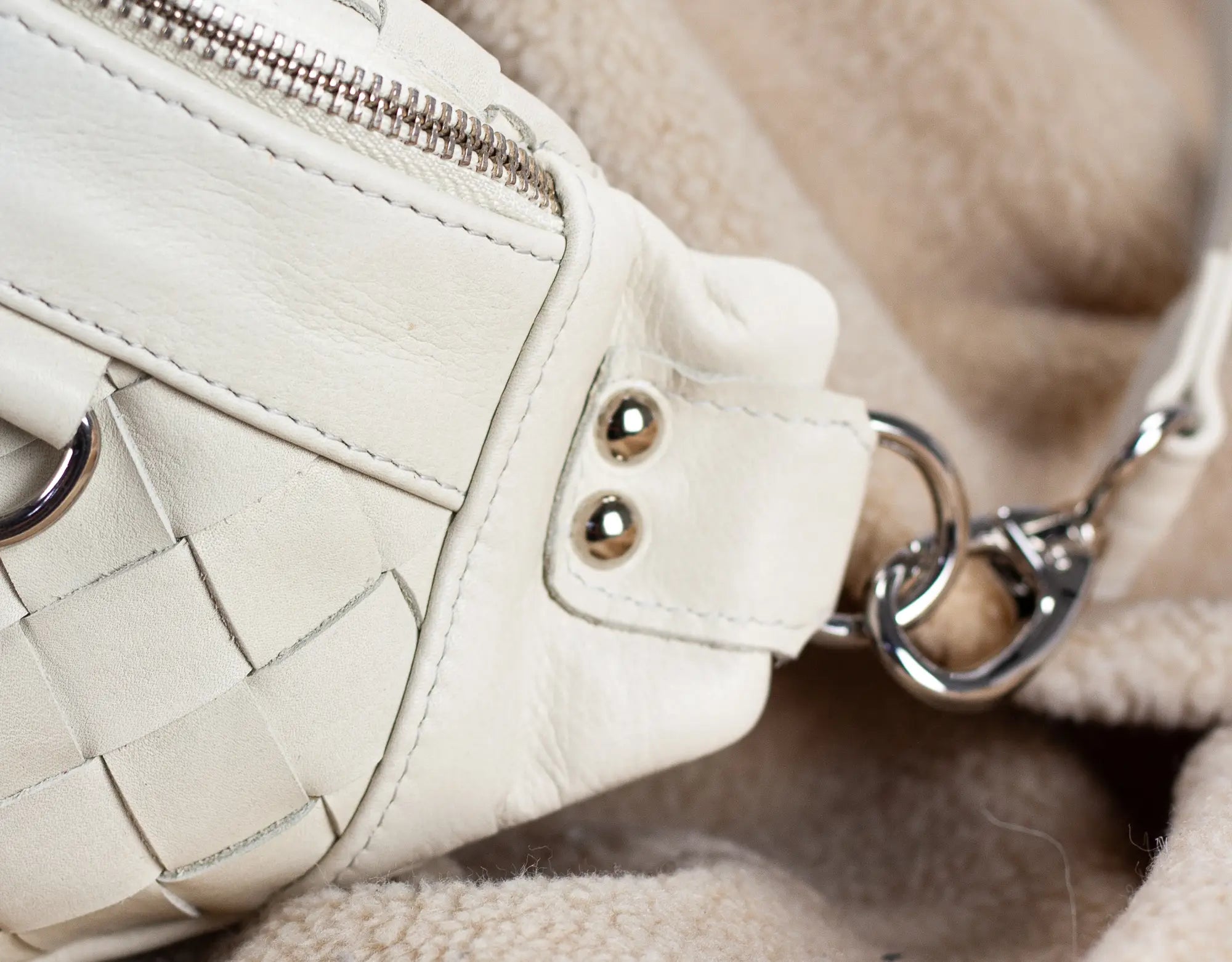 Close-up of a white woven handbag with a chain detail on a soft beige background