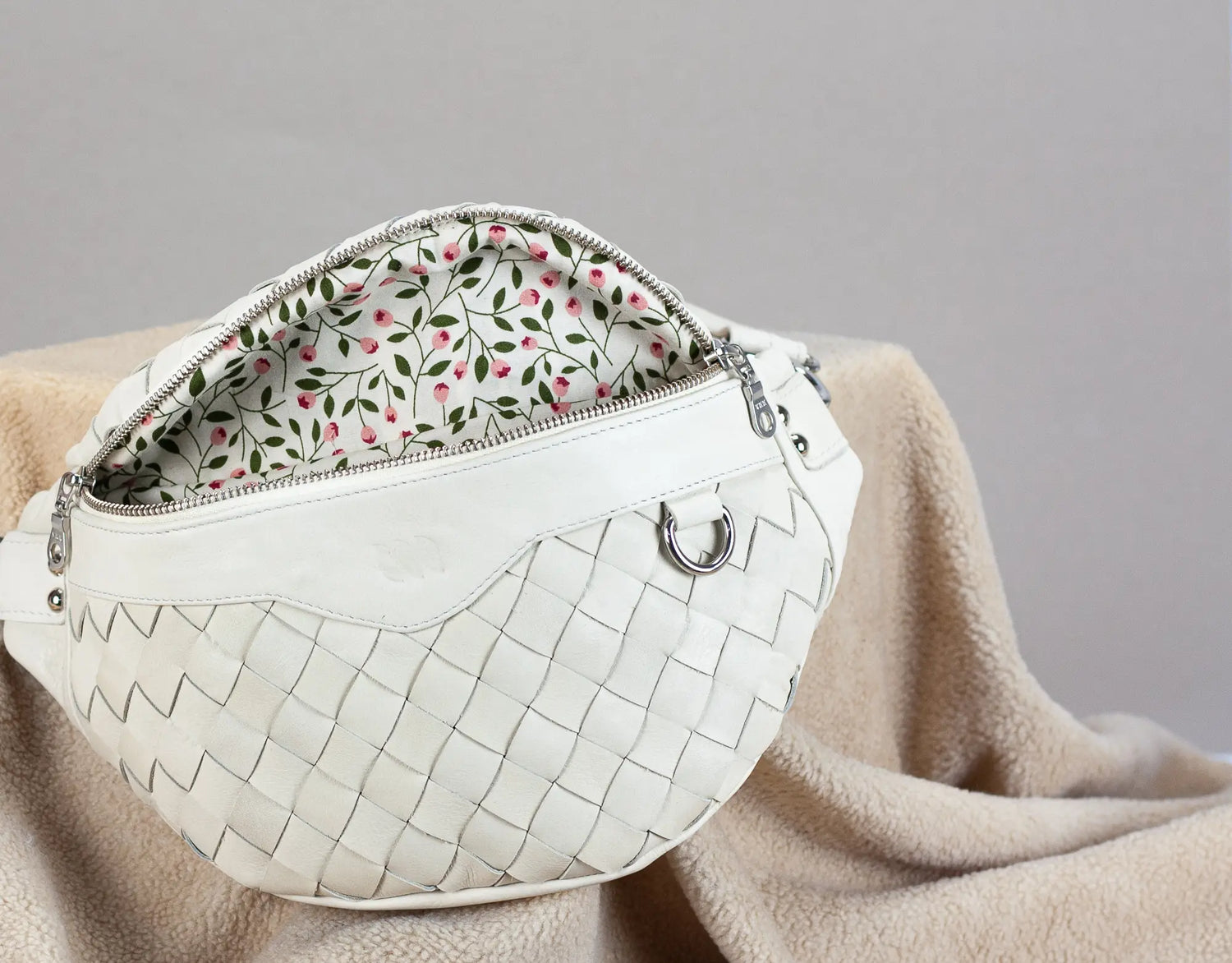 White handbag with floral interior on a beige blanket against a gray background