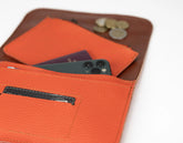 Orange leather wallet with phone, cards, and coins on a white background
