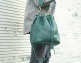 Green leather backpack held by a person against a textured white background