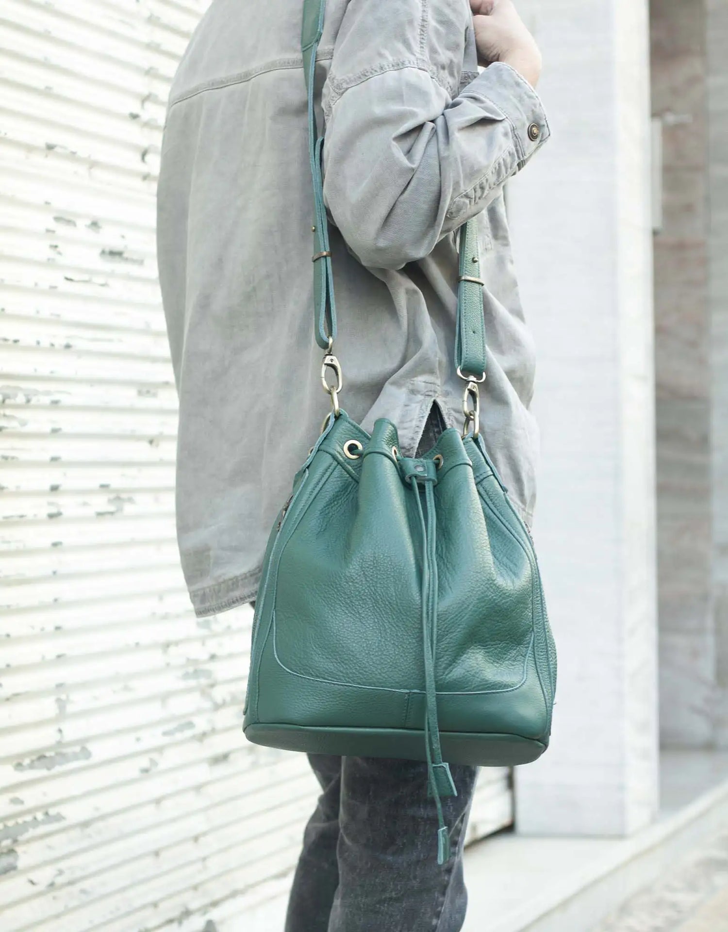 Person holding a green leather bucket bag against a light background