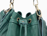 Close-up of a green leather handbag with gold hardware on a white background
