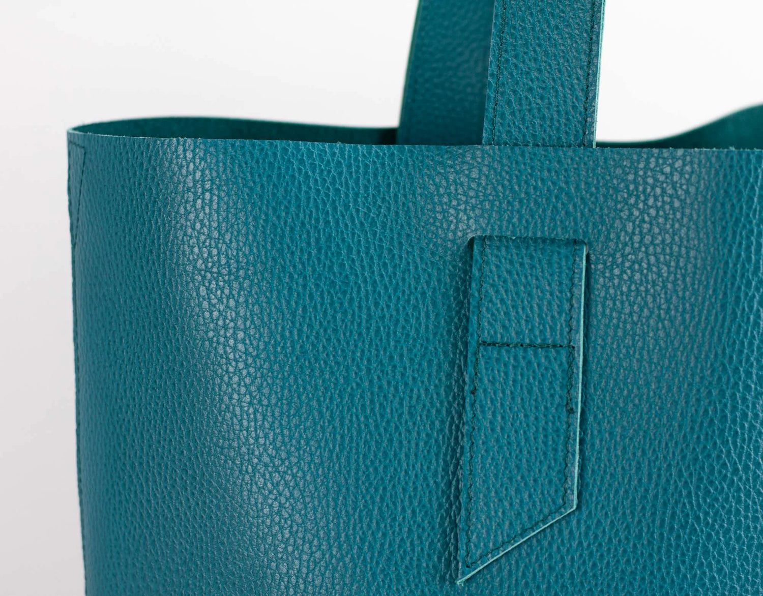 Teal leather tote bag with a pocket on a light gray background