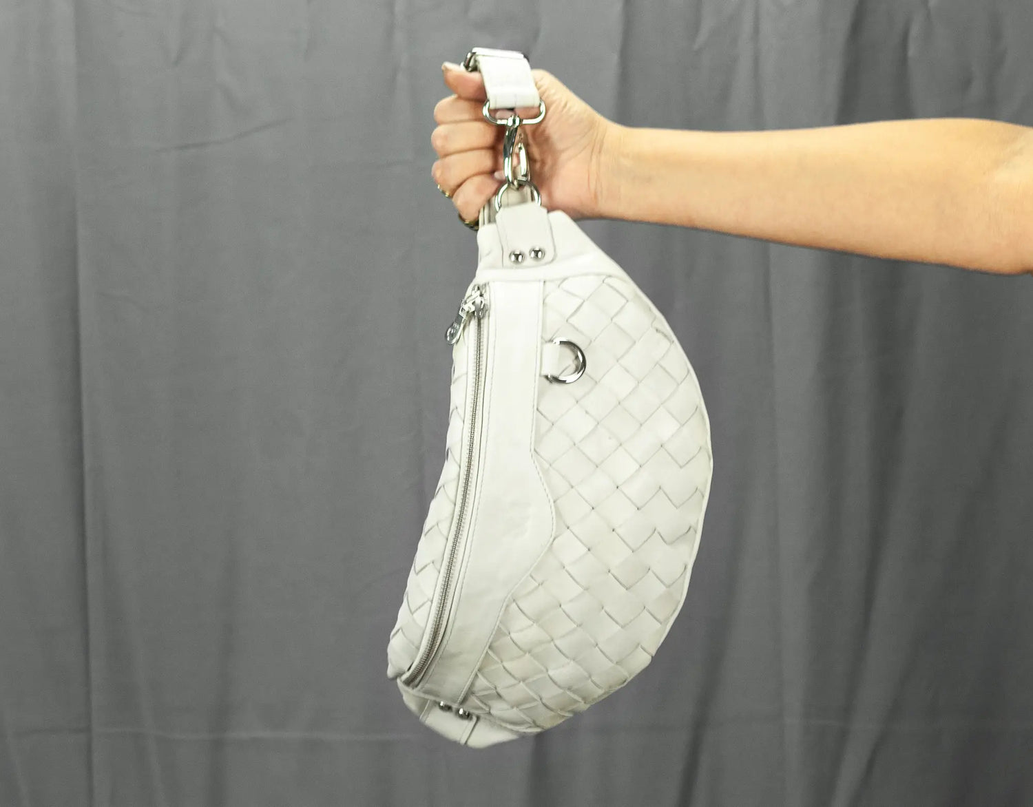 White quilted handbag held by a person against a gray background