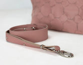 Pink leather dog leash with metal clip on a white surface, with a pink textured bag in the background.