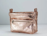 Rose gold metallic handbag with a zipper on a light gray background