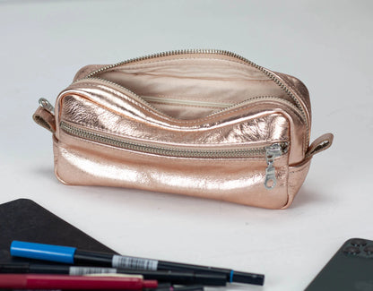 Rose gold metallic pouch with pens and a phone on a white background