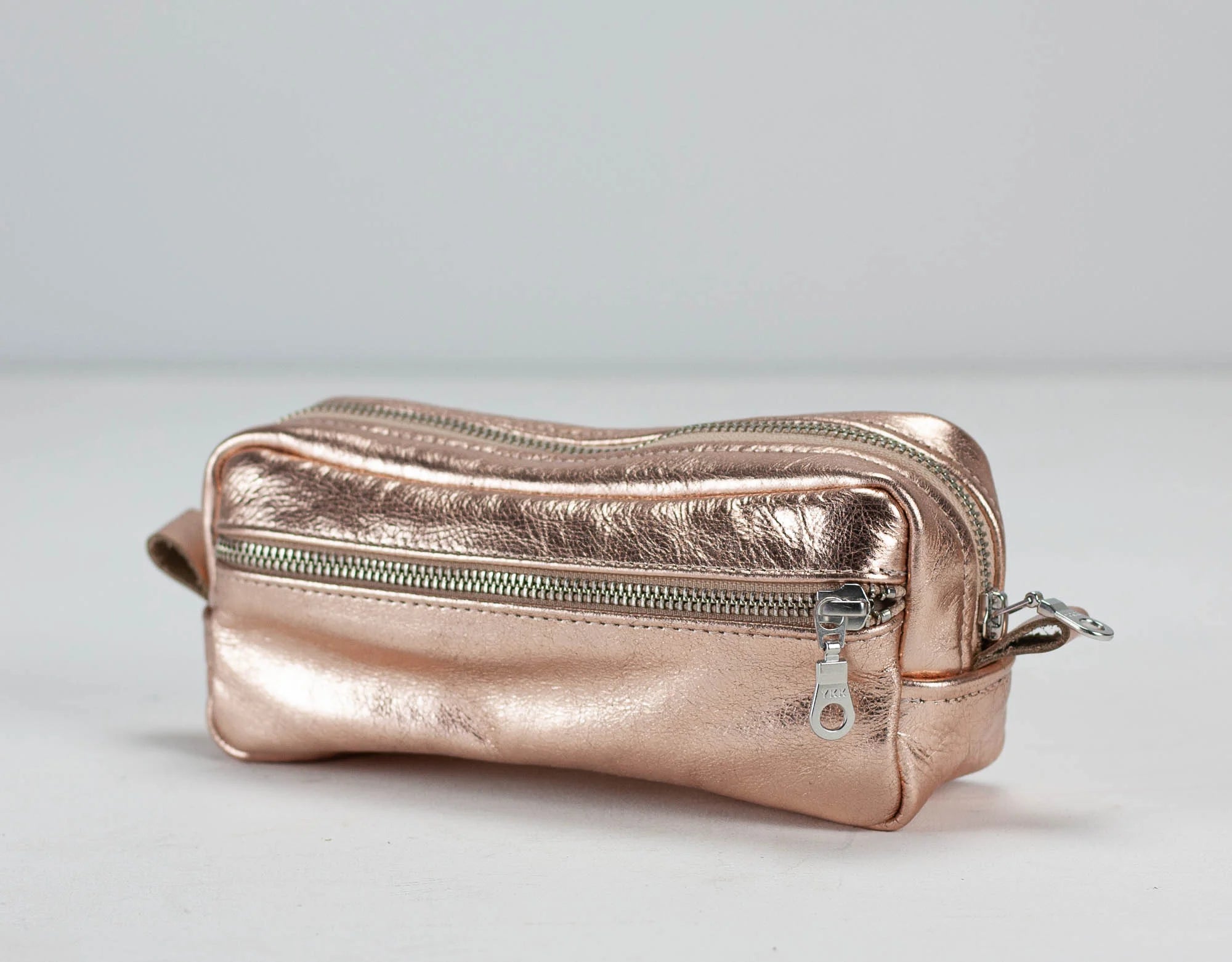 Rose gold metallic pouch with zipper on a light gray background
