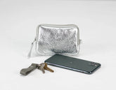 Silver metallic pouch, phone, and keys on a light gray background