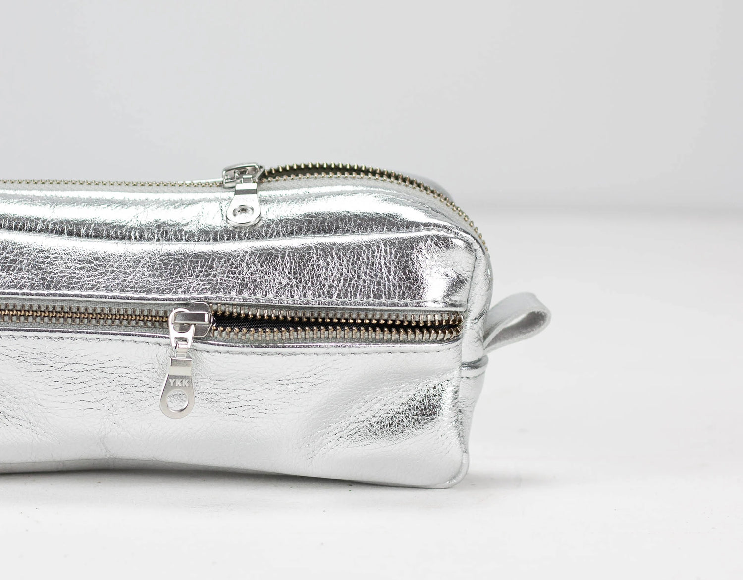 Silver metallic clutch bag with a zipper on a light gray background
