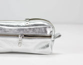 Silver metallic clutch bag with a zipper on a light gray background