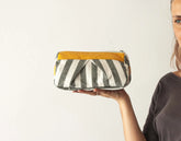 Person holding a striped pouch with a yellow top section against a plain background