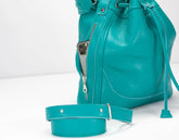 Turquoise leather bucket bag with a strap on a white background