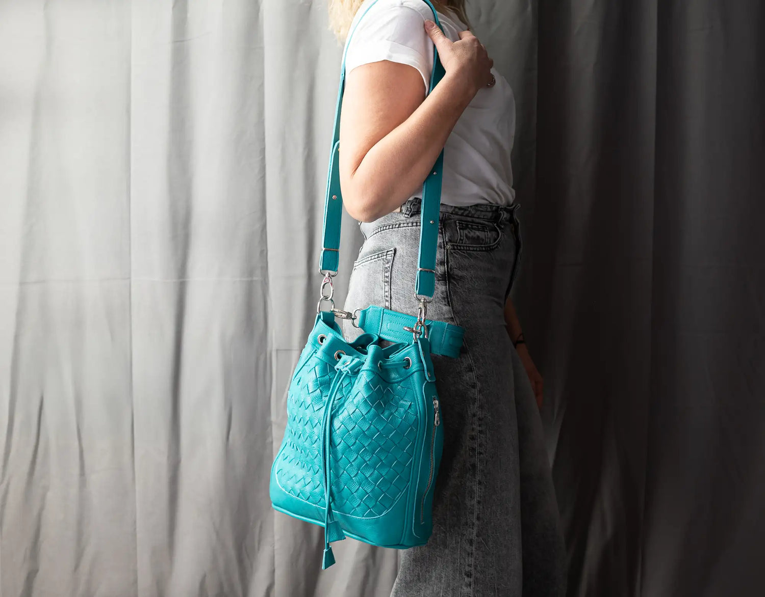Person wearing a turquoise quilted handbag with suspenders against a plain background