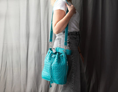 Person wearing a turquoise quilted handbag with suspenders against a plain background