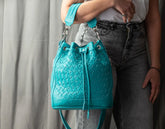 Turquoise woven handbag held by a person wearing gray jeans against a neutral background