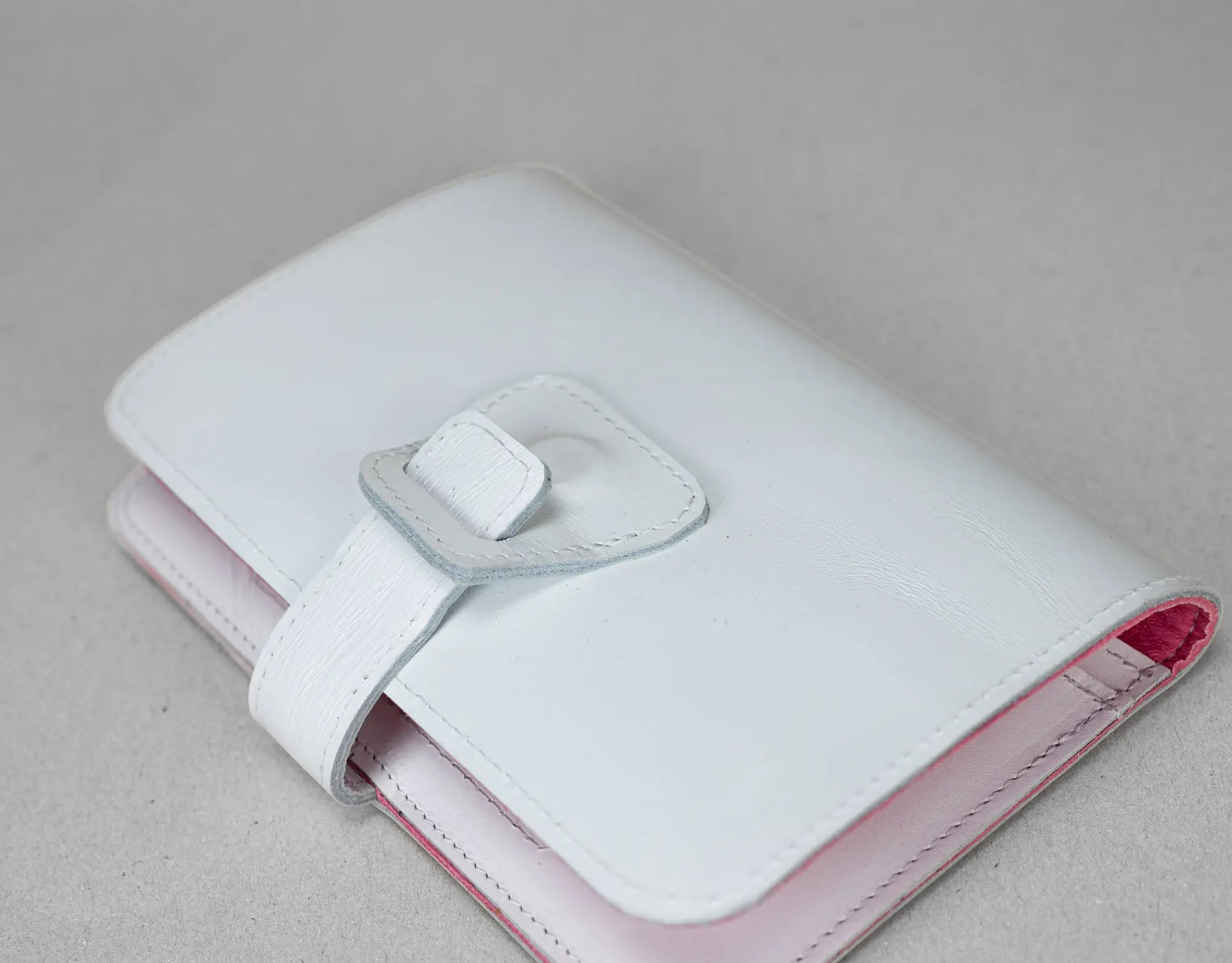 White and pink wallet with a silver buckle on a light gray background