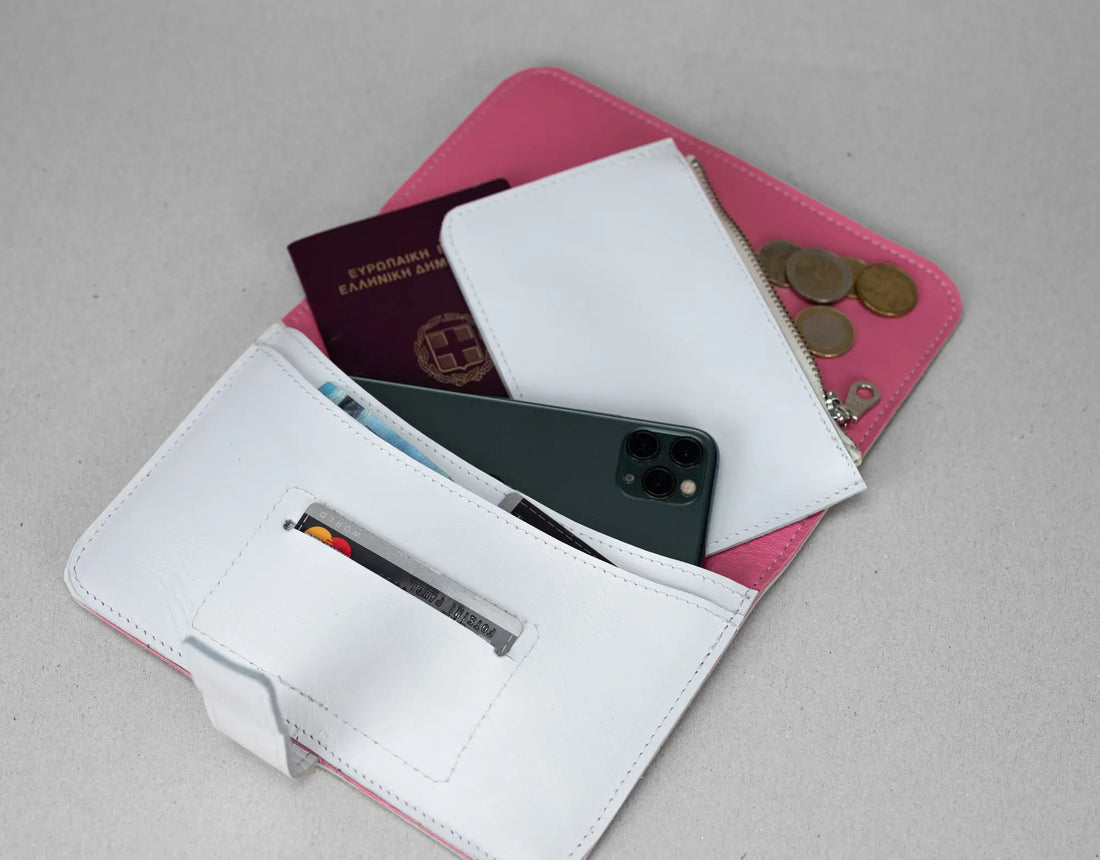 White wallet with pink interior, containing a phone, passport, and coins on a gray background