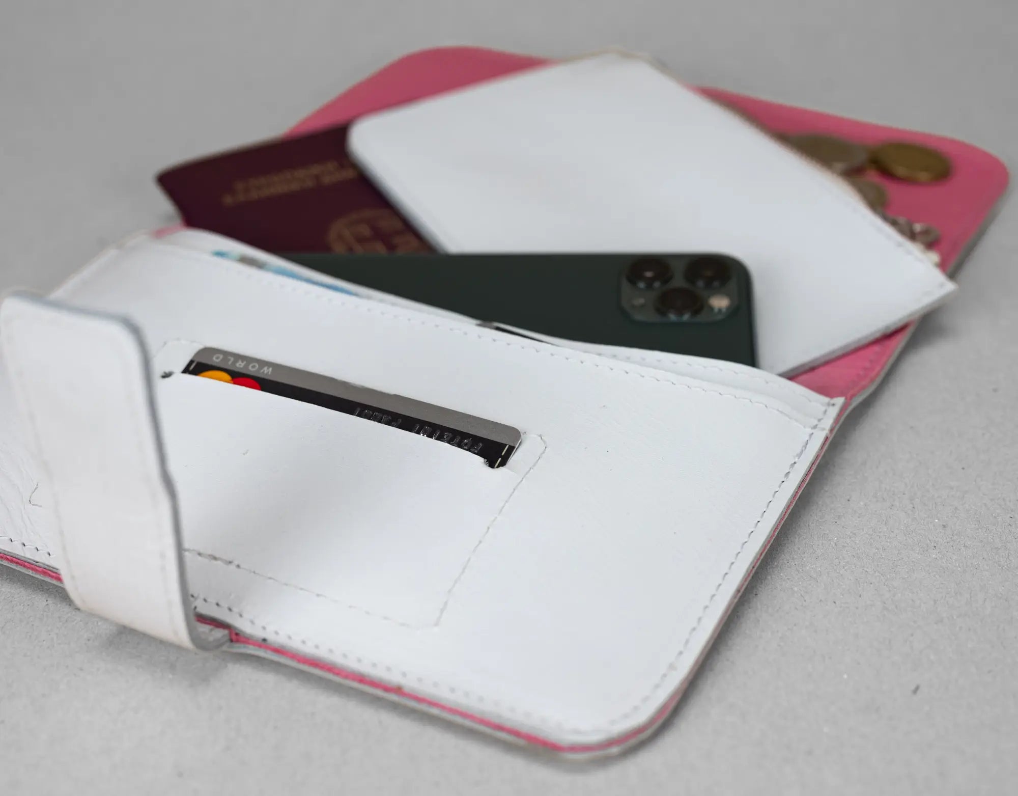 White wallet with phone, card, and passport on a gray surface