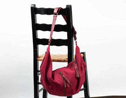 Red handbag with a strap on a black wooden chair against a white background